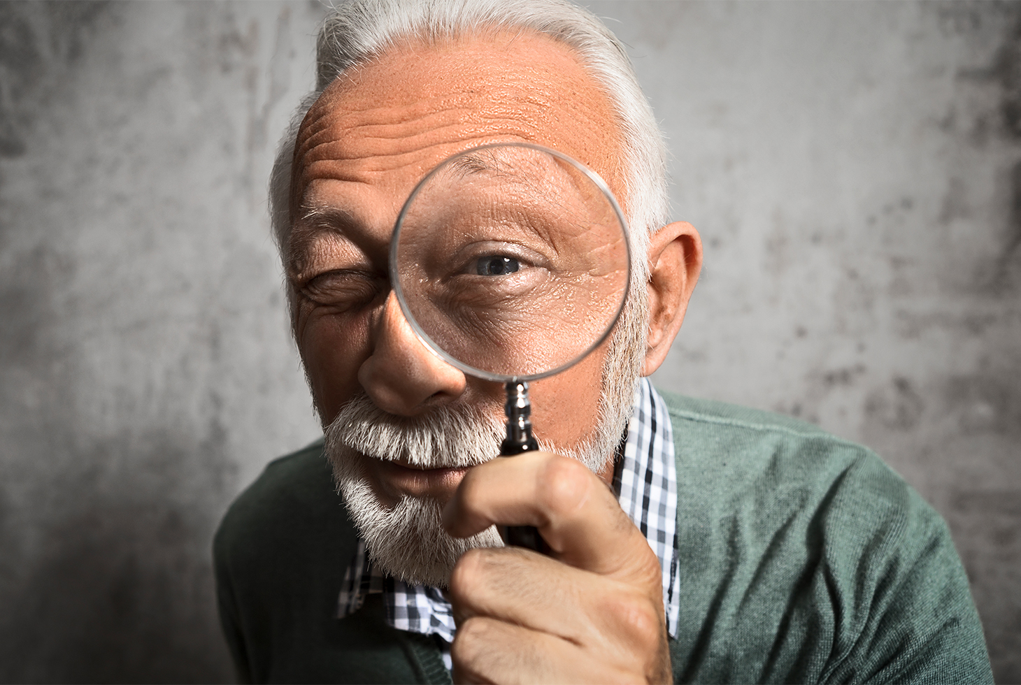 Portrait d’un senior regardant à travers une loupe. Visuel pour illustrer les questions les plus fréquentes sur l’incontinence
